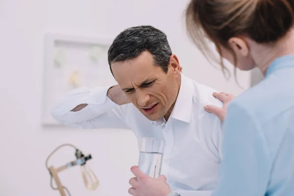 Mature businessman has neck pain while his colleague trying to help him at modern office — Stock Photo