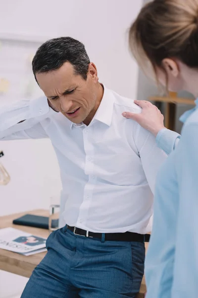 Hombre de negocios tiene dolor de cuello mientras que su colega tratando de ayudarle en la oficina moderna - foto de stock