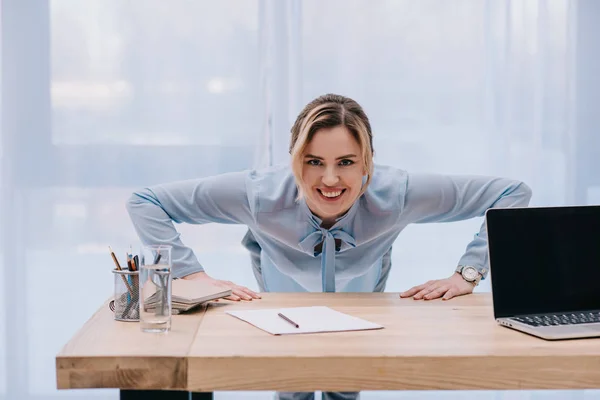 Glückliche Geschäftsfrau macht Liegestütze auf dem Tisch im Büro — Stockfoto