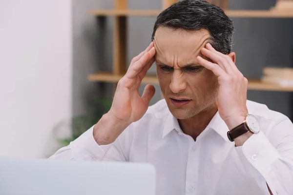 Mature businessman with painful migraine trying to work at office — Stock Photo
