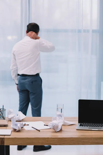 Reifer Geschäftsmann mit Nackenschmerzen im Büro mit chaotischem Arbeitsplatz im Vordergrund — Stockfoto