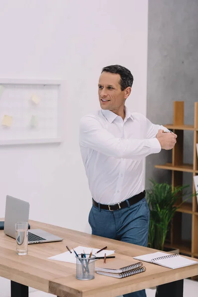 Healthy mature businessman stretching at his workplace in office — Stock Photo
