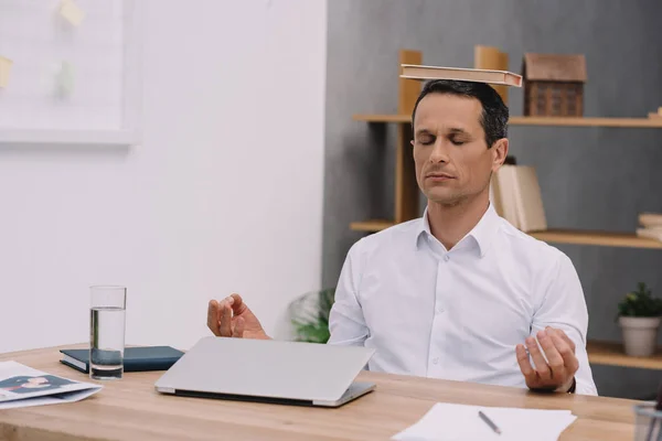 Calme homme d'affaires méditant avec livre sur la tête au bureau — Photo de stock