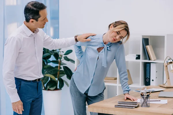 Attrayant femme d'affaires a mal au dos tandis que son collègue essaie de l'aider au bureau — Photo de stock