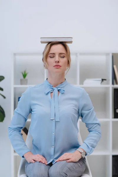 Bela mulher de negócios meditando com livro na cabeça no escritório — Fotografia de Stock