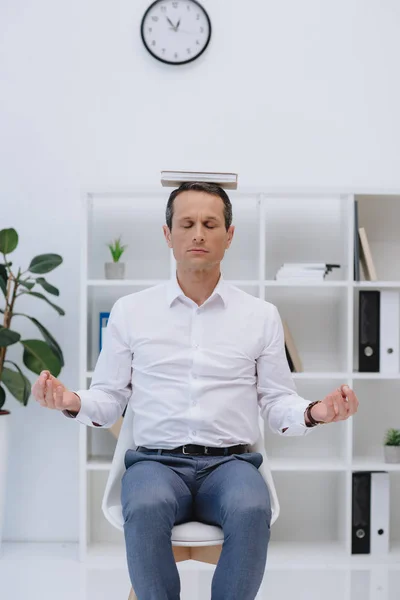 Geschäftsmann meditiert im Büro mit Buch auf dem Kopf — Stockfoto