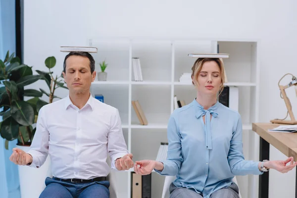 Empresários meditando com livros na cabeça no escritório moderno — Fotografia de Stock