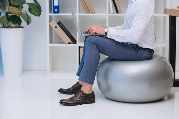 Cropped shot of businessman working with laptop while sitting on fit ball — Stock Photo