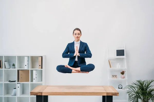 Jovem empresária com olhos fechados meditando enquanto levita no local de trabalho — Fotografia de Stock