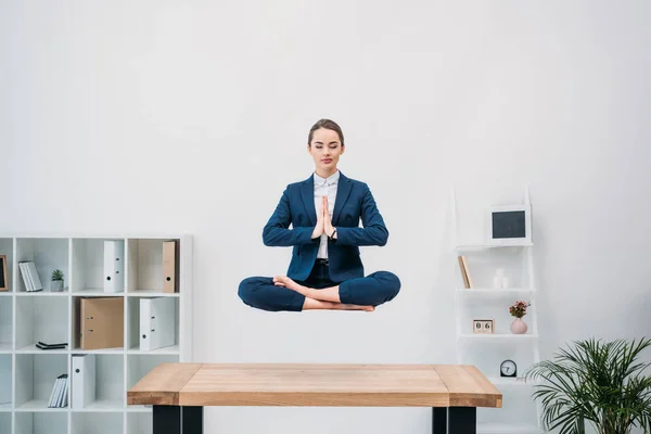 Giovane donna d'affari con gli occhi chiusi meditando mentre levita sul posto di lavoro — Foto stock