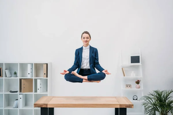 Усміхнена молода бізнес-леді з закритими очима медитує під час вирівнювання на робочому місці — стокове фото
