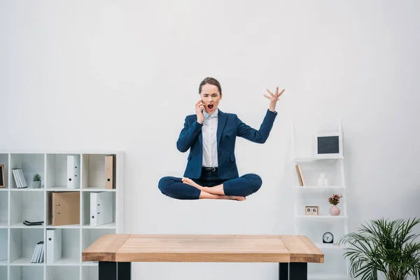 Jovem empresária emocional falando por smartphone enquanto levita no escritório — Fotografia de Stock