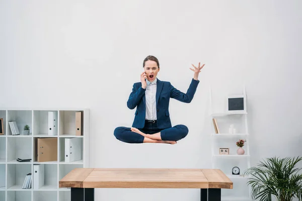 Jeune femme d'affaires émotionnelle parlant par smartphone tout en lévitant dans le bureau — Photo de stock