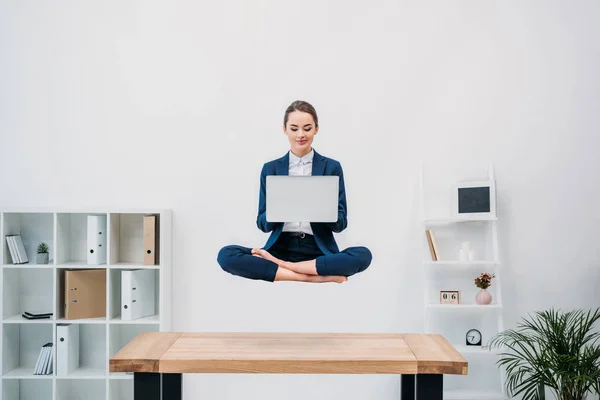 Smiling young businesswoman using laptop while levitating in office — Stock Photo