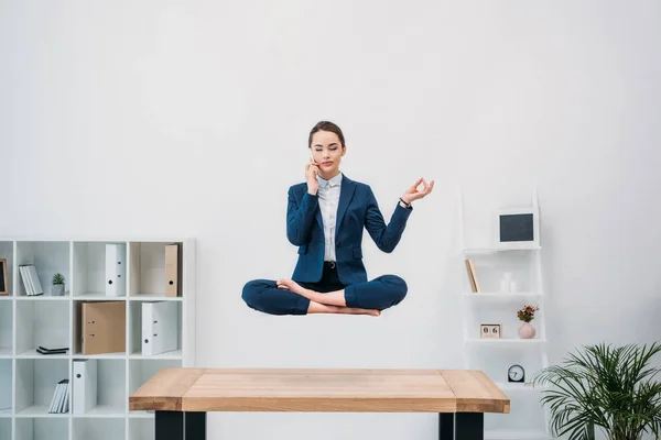 Empresária falando por smartphone enquanto levita no escritório — Fotografia de Stock