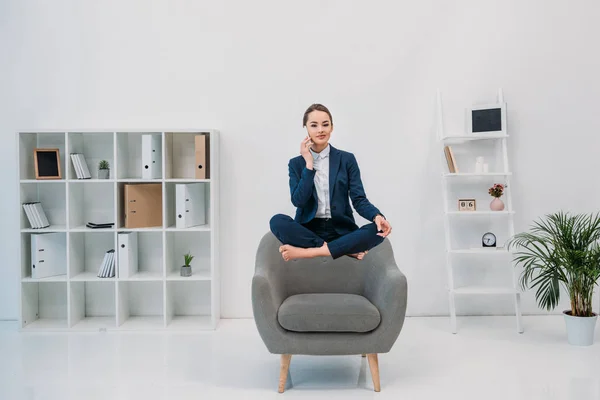 Young businesswoman talking by smartphone and smiling at camera while levitating in office — Stock Photo