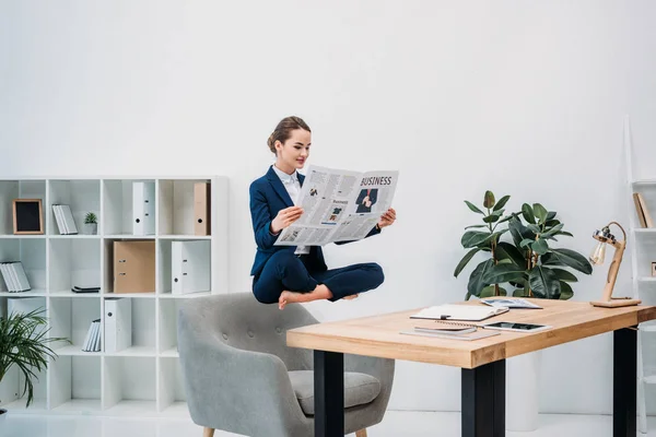 Sonriente joven empresaria leyendo el periódico mientras levita en el lugar de trabajo - foto de stock