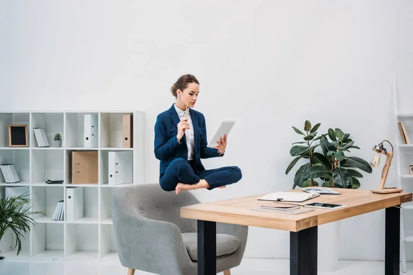 Mujer de negocios que usa tableta digital mientras levita en el lugar de trabajo - foto de stock