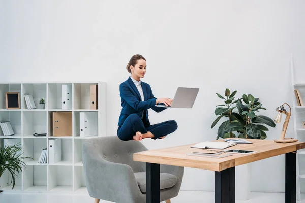Mujer de negocios que usa el ordenador portátil mientras levita en el lugar de trabajo - foto de stock