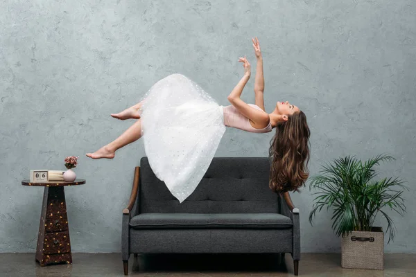 Schöne junge barfüßige Frau schwebt über Sofa — Stockfoto