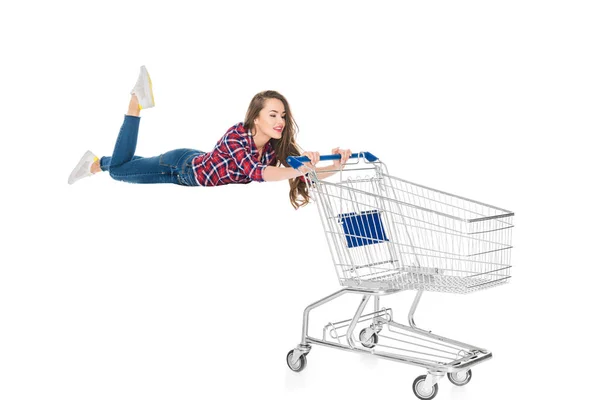 Lächelnde junge Frau schwebt mit leerem Einkaufswagen auf weißem Grund — Stockfoto