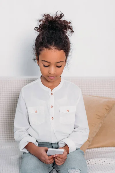 Adorabile bambino africano americano utilizzando smartphone sul divano — Foto stock