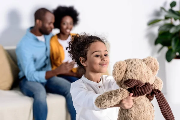 Africana americana hija jugando con teddy oso en casa - foto de stock