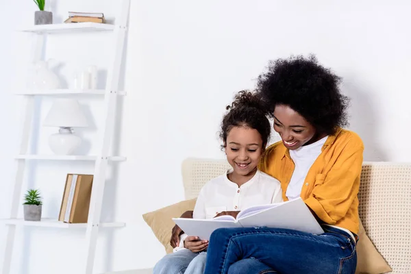 Glücklich afrikanisch-amerikanische Mutter und Tochter lesen gemeinsam Buch zu Hause — Stockfoto