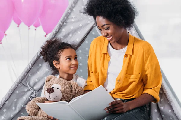 Feliz afroamericano madre e hija leyendo libro juntos en casa - foto de stock