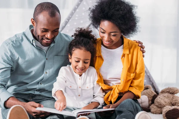 Feliz afroamericano hija leyendo para padres en casa - foto de stock