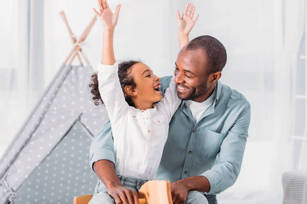 Sorrindo afro-americano pai e filha se divertindo e olhando um para o outro em casa — Fotografia de Stock
