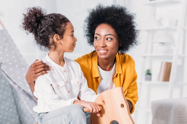 Afro-americana mãe e filha abraçando filha no cavalo de balanço em casa — Fotografia de Stock