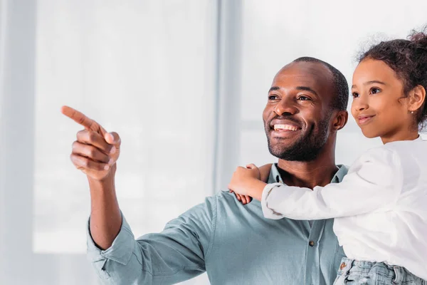 Усміхнений афроамериканський батько вказує на щось дочці — стокове фото