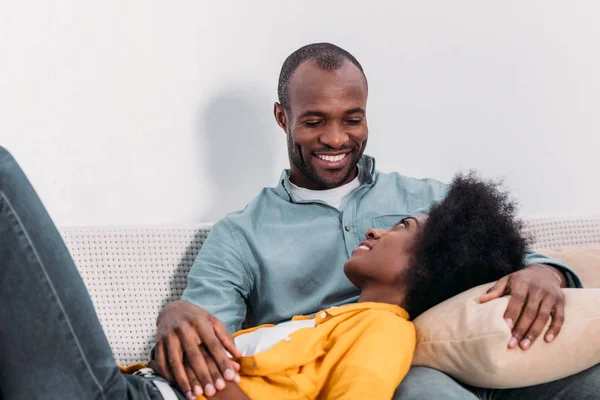 Africano americano novia mintiendo en novios piernas en sofá en casa - foto de stock