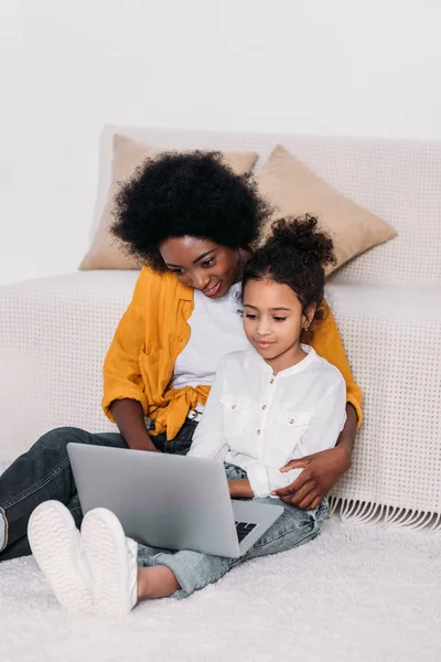 Afro-américaine mère et fille câlins et regarder quelque chose à l'ordinateur portable — Photo de stock