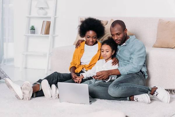 Africanos americanos padres y hija viendo película en el ordenador portátil en casa - foto de stock