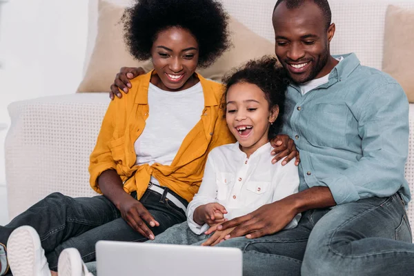 Riéndose africanos americanos padres y hija viendo película en portátil - foto de stock