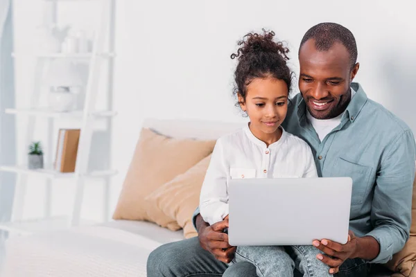 Padre y la hija afroamericanos felices usando el ordenador portátil en casa - foto de stock