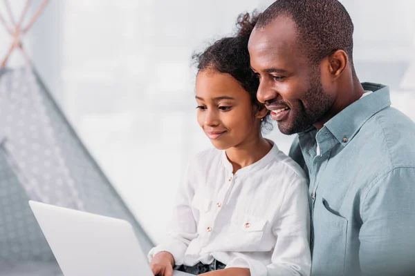 Side view of happy african american father and daughter using laptop at home — Stock Photo