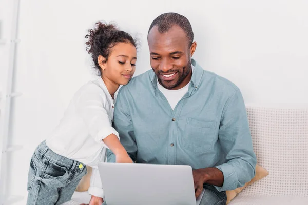 Afro-americana figlia mostrando qualcosa sul computer portatile al padre a casa — Foto stock