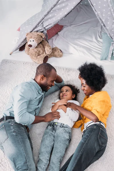 Vue grand angle des parents afro-américains et fille s'amuser sur le sol à la maison — Photo de stock