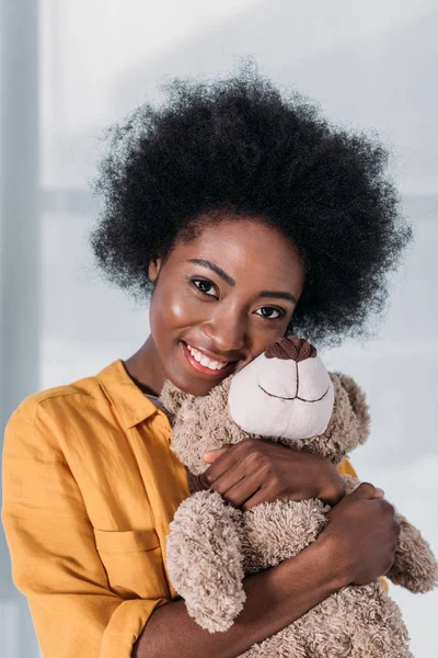 Sorrindo mulher afro-americana com ursinho de pelúcia em casa — Fotografia de Stock