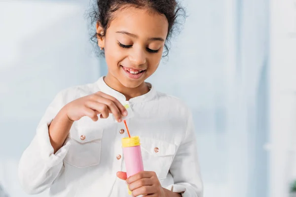 Sonriente adorable africano americano niño haciendo jabón burbujas en casa - foto de stock