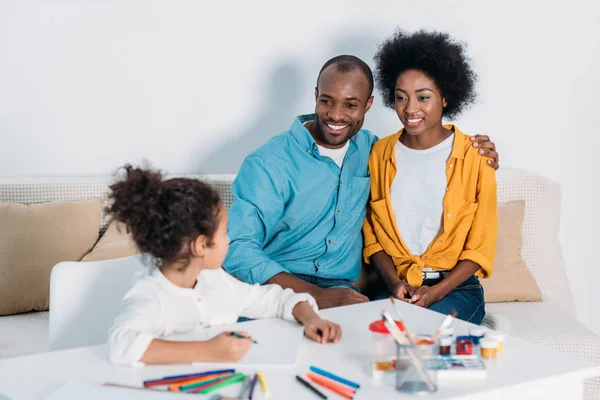 Афроамериканські батьки дивляться на дочку малюють вдома — стокове фото