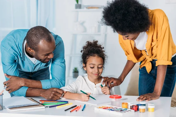 Afroamericanos padres ayudar hija dibujo en casa - foto de stock