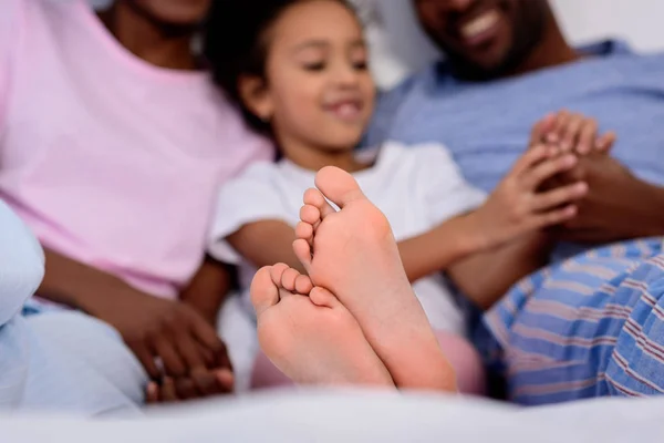 Africani genitori americani e figlia sdraiati sul letto con i piedi in primo piano — Foto stock
