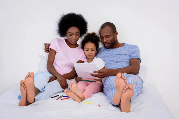 African american parents and daughter looking at painting album at home — Stock Photo