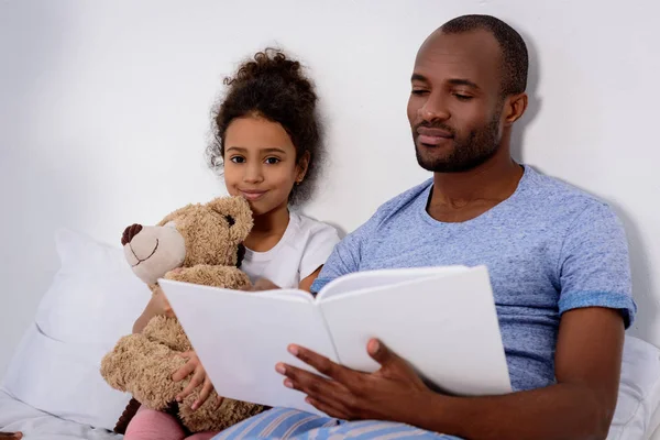African american father reading book for daughter at home — Stock Photo