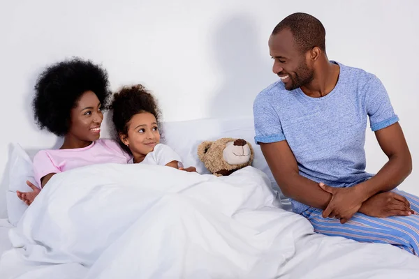 Afroamericanos padres e hija en dormitorio mirándose entre sí - foto de stock