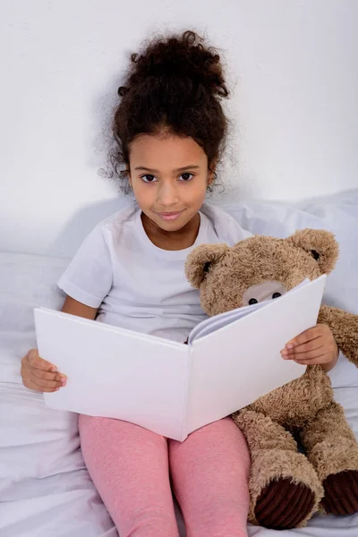 Entzückendes afrikanisch-amerikanisches Kind hält Buch in der Hand und schaut zu Hause in die Kamera — Stockfoto